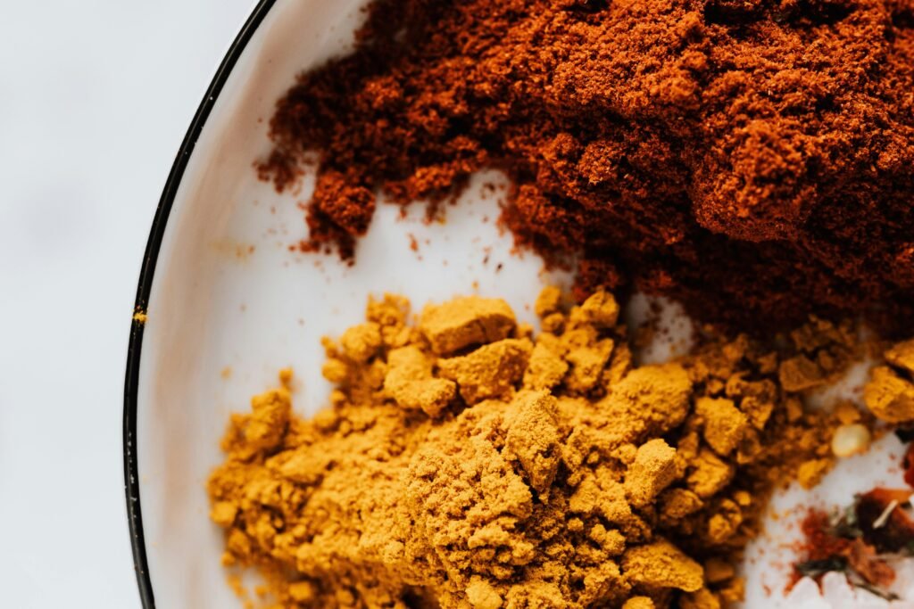 Top view of small heaps of ground chili and curcuma powders in metal bowl on white surface