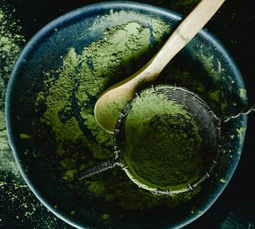 pexels-photo-6834163-6834163 Overhead view of green matcha powder with a wooden spoon in a dark blue ceramic bowl, showcasing a rustic kitchen style.